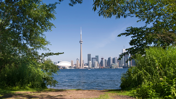 Toronto skyline and CN Tower viewed from across Lake Ontario, representing the GTA real estate market in June 2025 with rising listings, shifting prices, and buyer opportunities.