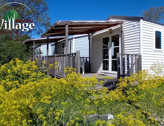 Mobile home blanc "Village" avec terrasse en bois et fleurs jaunes.