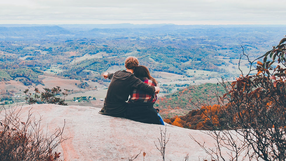 White straight couple sitting on a cliff overlooking a town during the fall