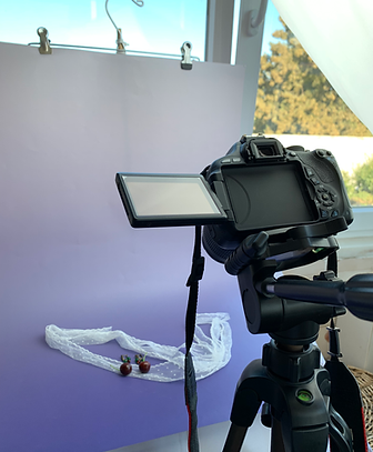 Camera on a tripod photographing miniature earrings against a purple backdrop