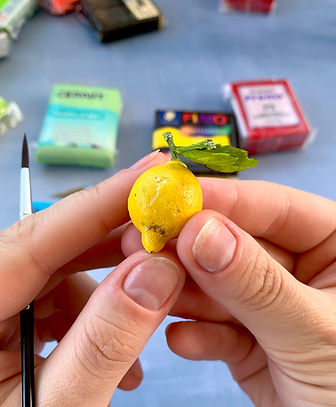 Hands sculpting a miniature lemon with green leaves