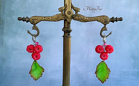 Handmade raspberry earrings with green leaves on a jewelry stand