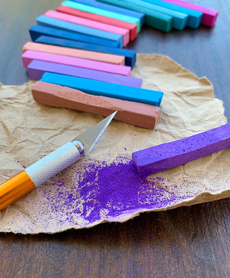 Colourful pigment sticks and craft knife beside purple pigment dust