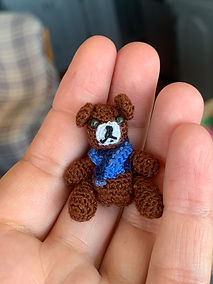 Tiny crocheted teddy bear with a blue scarf resting in a hand