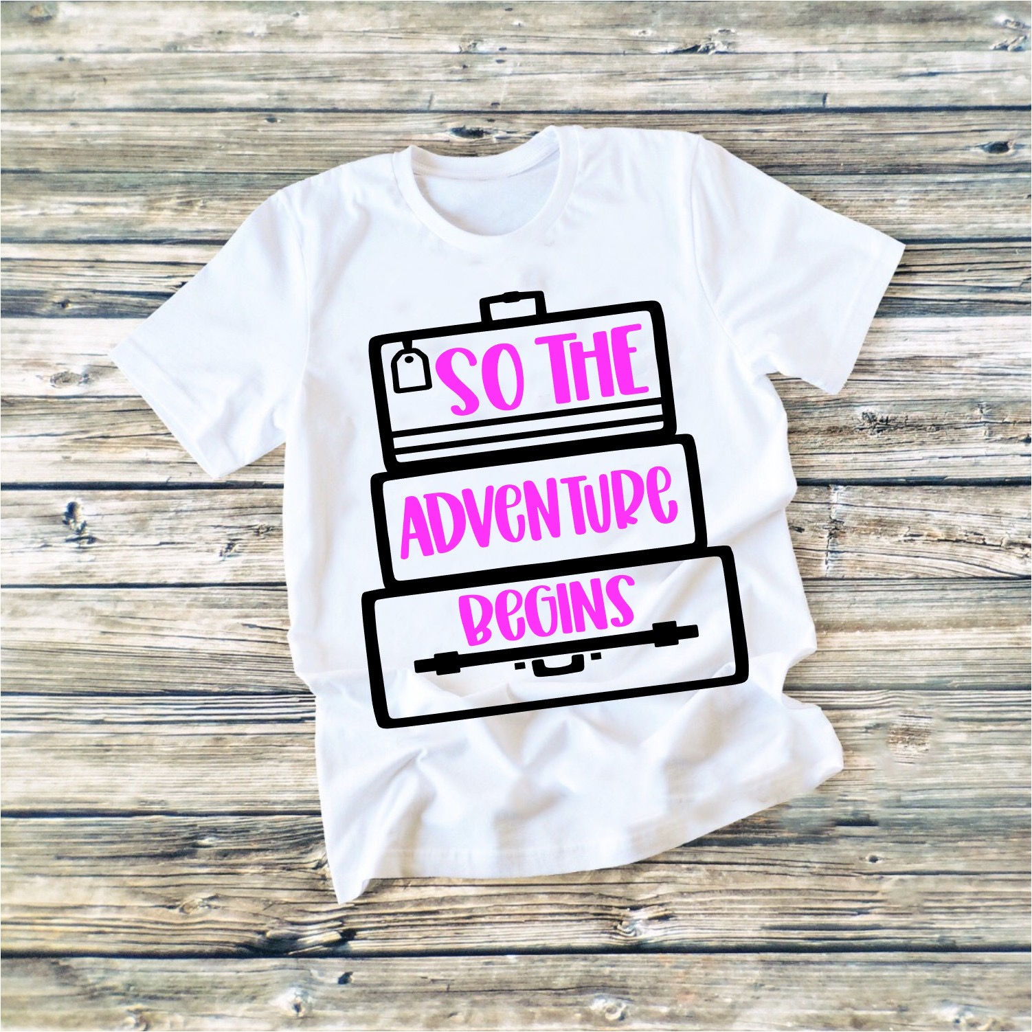 White t-shirt with text reading So The Adventure Begins contained within graphics meant to look like bags.