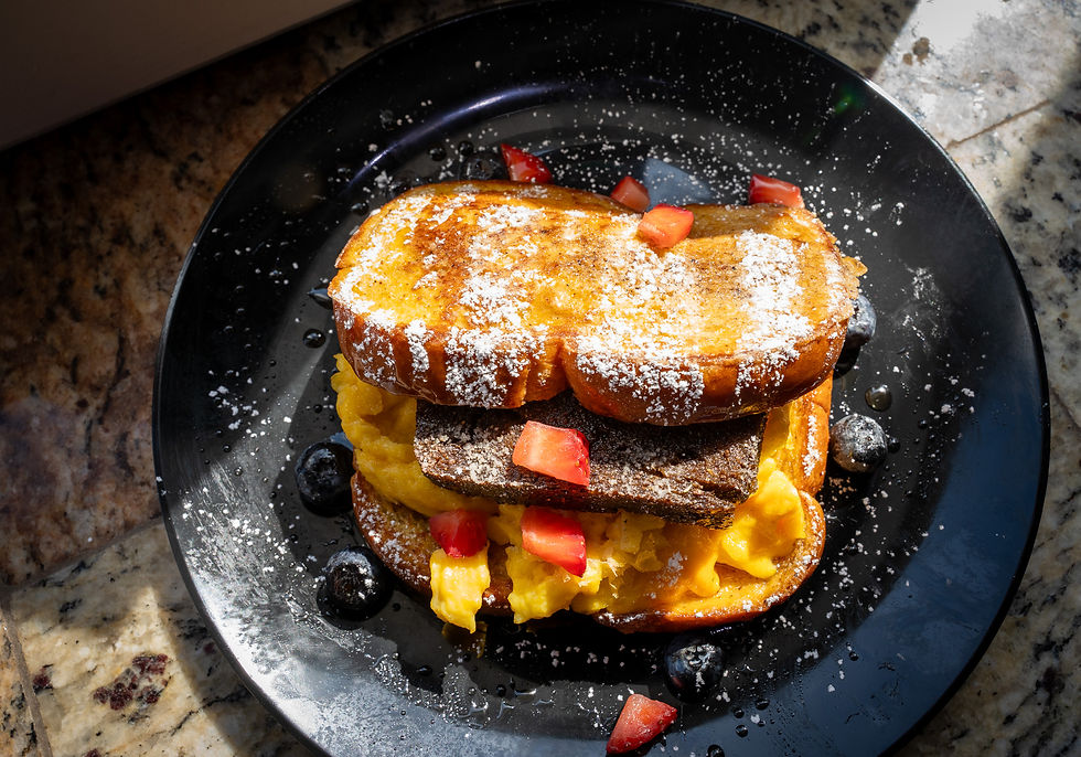French toast topped with powdered sugar, diced tomatoes, and blueberries on a black plate with a granite background, sunlit atmosphere.