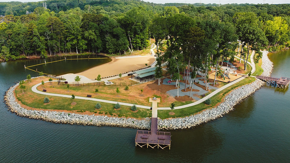 Aerial view of a wooded lakeside park with winding paths, a sandy beach, playground, and docks on calm water.