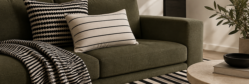 Modern Airbnb living room featuring an olive green sofa with layered black and white striped cushions, a textured striped throw blanket, and a geometric striped rug.