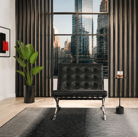 Contemporary minimalist sitting area inspired by American Psycho, featuring a black leather chair, vertical wall panels, and floor-to-ceiling windows.