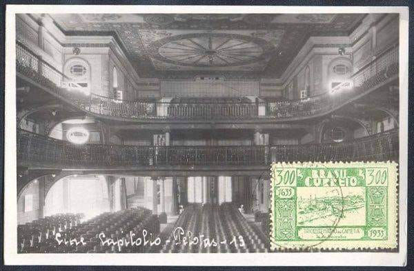 Fotografia histórica em preto e branco do interior do Cine Capitólio de Pelotas, mostrando a sala principal com três níveis de plateia e mezanino, fileiras de poltronas, balcões com balaustradas ornamentadas, teto decorativo com rosácea central, colunas e arcos clássicos. Imagem em formato de cartão postal com selo verde do correio brasileiro.