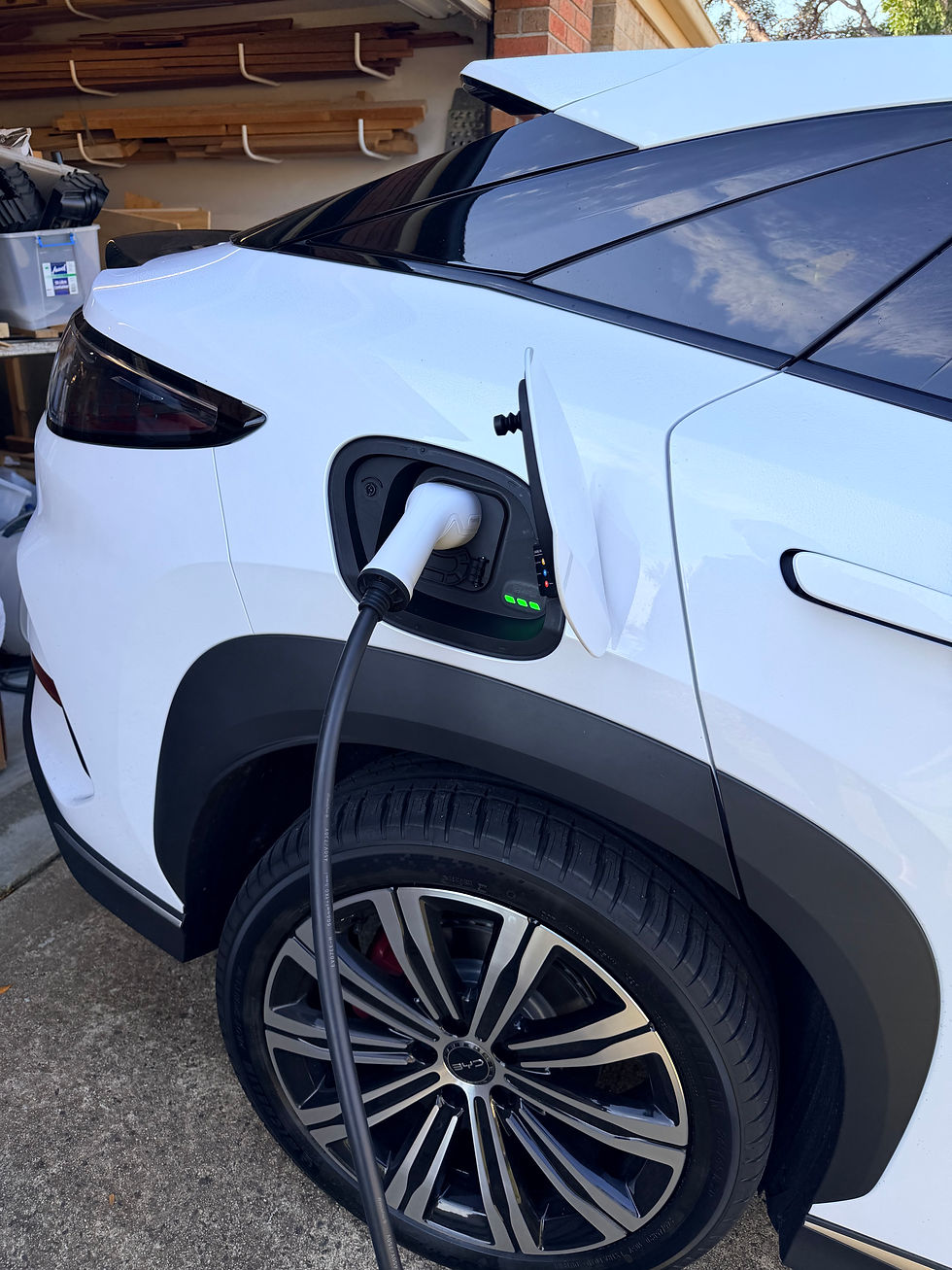 Zappi tethered connector plugged into the charge port of a white BYD Sealion 7 parked in the driveway.