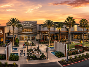 Sunset over La Plaza mall with palm trees, shoppers, and lit restaurant signs for Palenque Grill, Yard House, and Casa Mure.