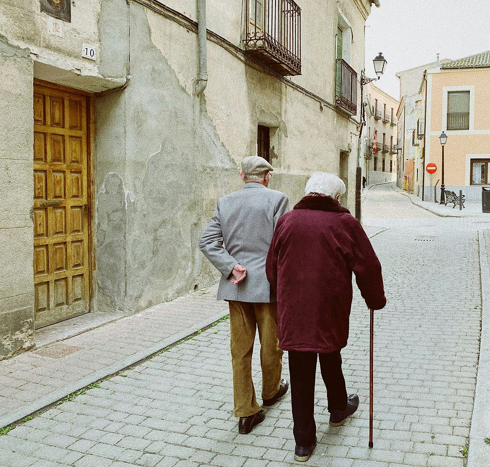 Elderly couple walking down a cobblestone street, one with a cane. Rustic buildings and muted colors create a nostalgic, peaceful mood.