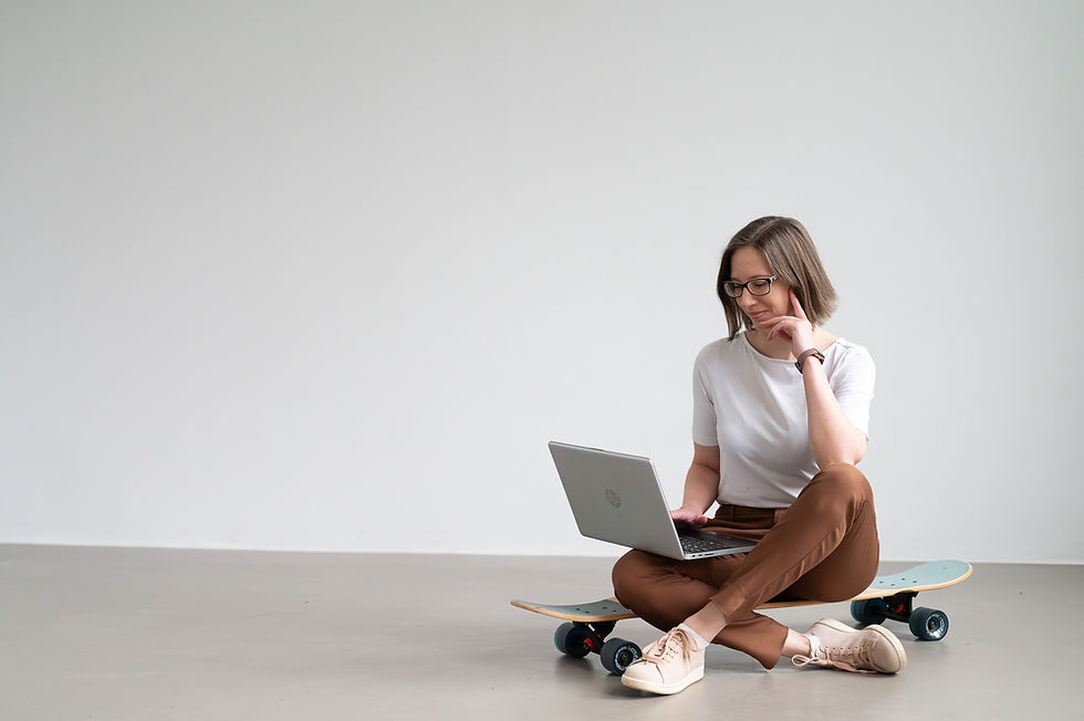 Eine Frau im business casual Outfit sitzt lässig auf ihrem Skateboard mit einem Laptop auf ihrem Schoß. Die Umgebung ist klar gehalten mit grauem Betonboden und weißer Wand. Das Bild ist bei einer Mini Brand Shooting Experience von Christiane Timm Brand Fotografie & Markenstrategie, einer Personal Branding Fotografin in Lüneburg und Hamburg entstanden.