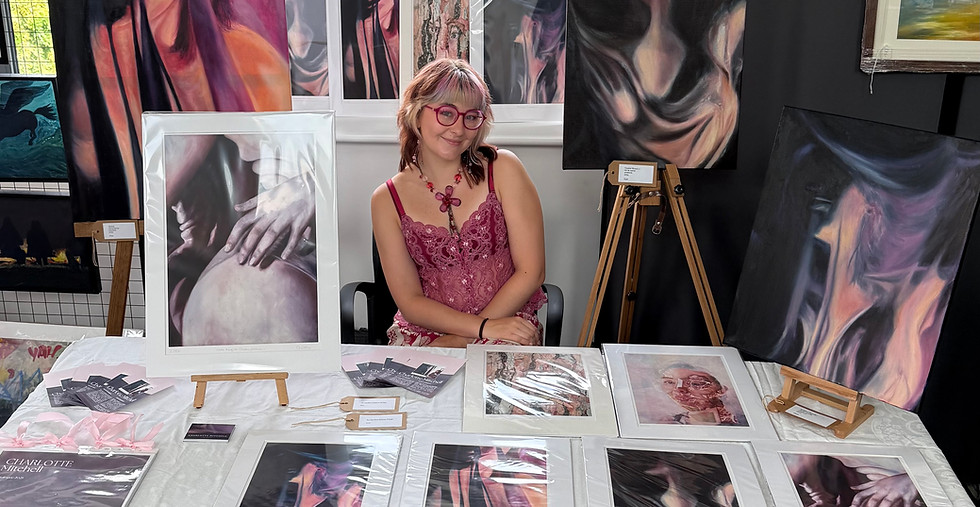 Photo of Charlotte Mitchell at an art market surrounded by original oil paintings and fine art prints.