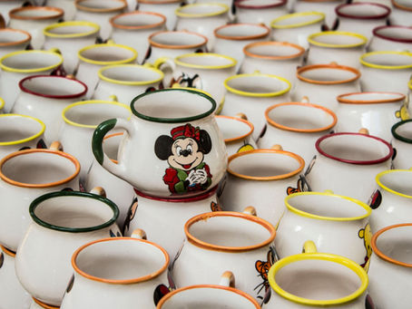 Rows of white Disney mugs with colourful rims, centered Minnie Mouse mug in front, arranged tightly on a table.