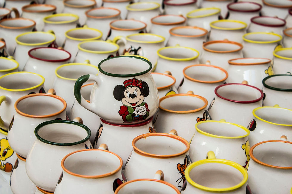 Rows of white Disney mugs with colourful rims, centered Minnie Mouse mug in front, arranged tightly on a table.