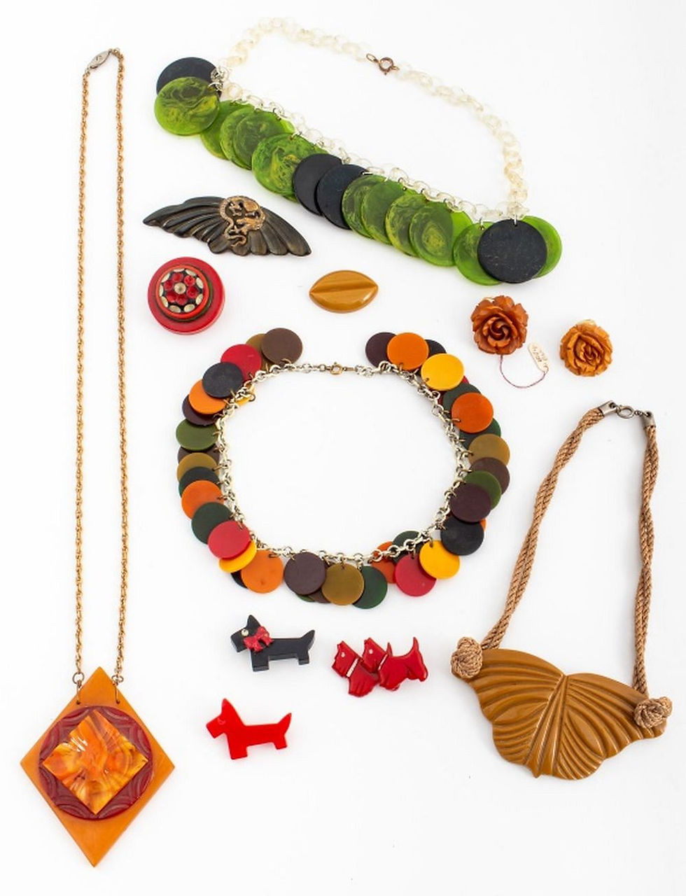 Assorted colourful vintage bakelite necklaces, brooches, and earrings laid out on white background featuring green discs, bold circles, and leaf-shaped pendants