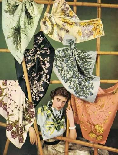 Woman poses among colourful Jacqmar floral scarves draped on a bamboo frame, in a vintage fashion editorial.