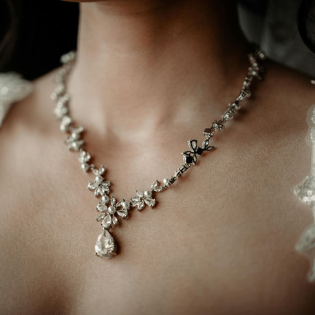 Close-up of a woman’s neck and chest in a lace dress, wearing a sparkling floral vintage necklace with a teardrop pendant.