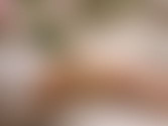 Wrist adorned with gold vintage bracelets and a diamond band, set against a blurred floral background. A white cup on the table adds elegance.