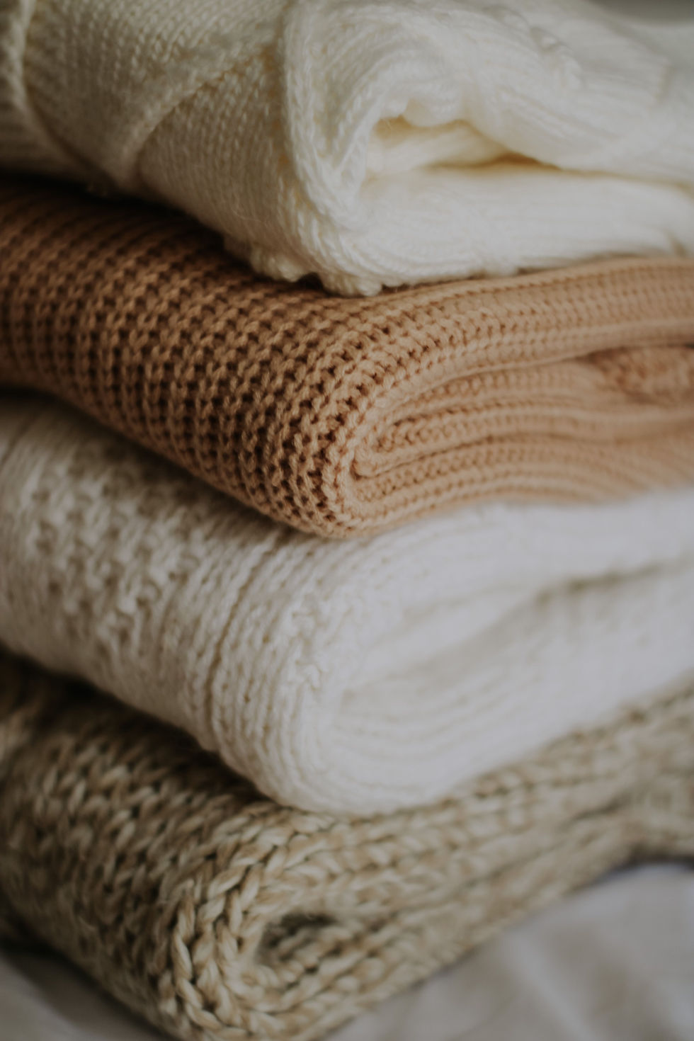 Neatly folded cream and neutral knitwear, illustrating the correct way to store knitted garments without stretching them.