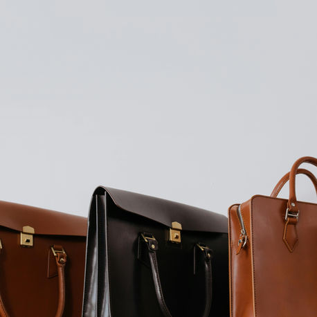 Three leather briefcases in brown and black are arranged against a plain white background. They feature gold and silver hardware.