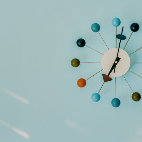 Colourful mid-century modern wall clock with multicolored balls on a pale blue wall, hands near 5:10.