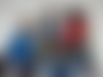 Four people in colourful retro track jackets, sitting against a white wall, wearing sunglasses. The mood is relaxed and casual.