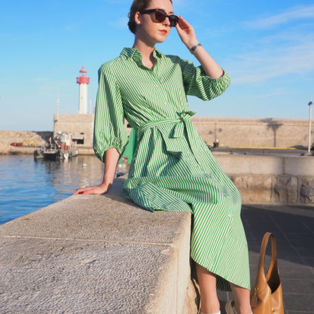 woman wearing a green shirtwaister dress, sitting on a wall at the harbour