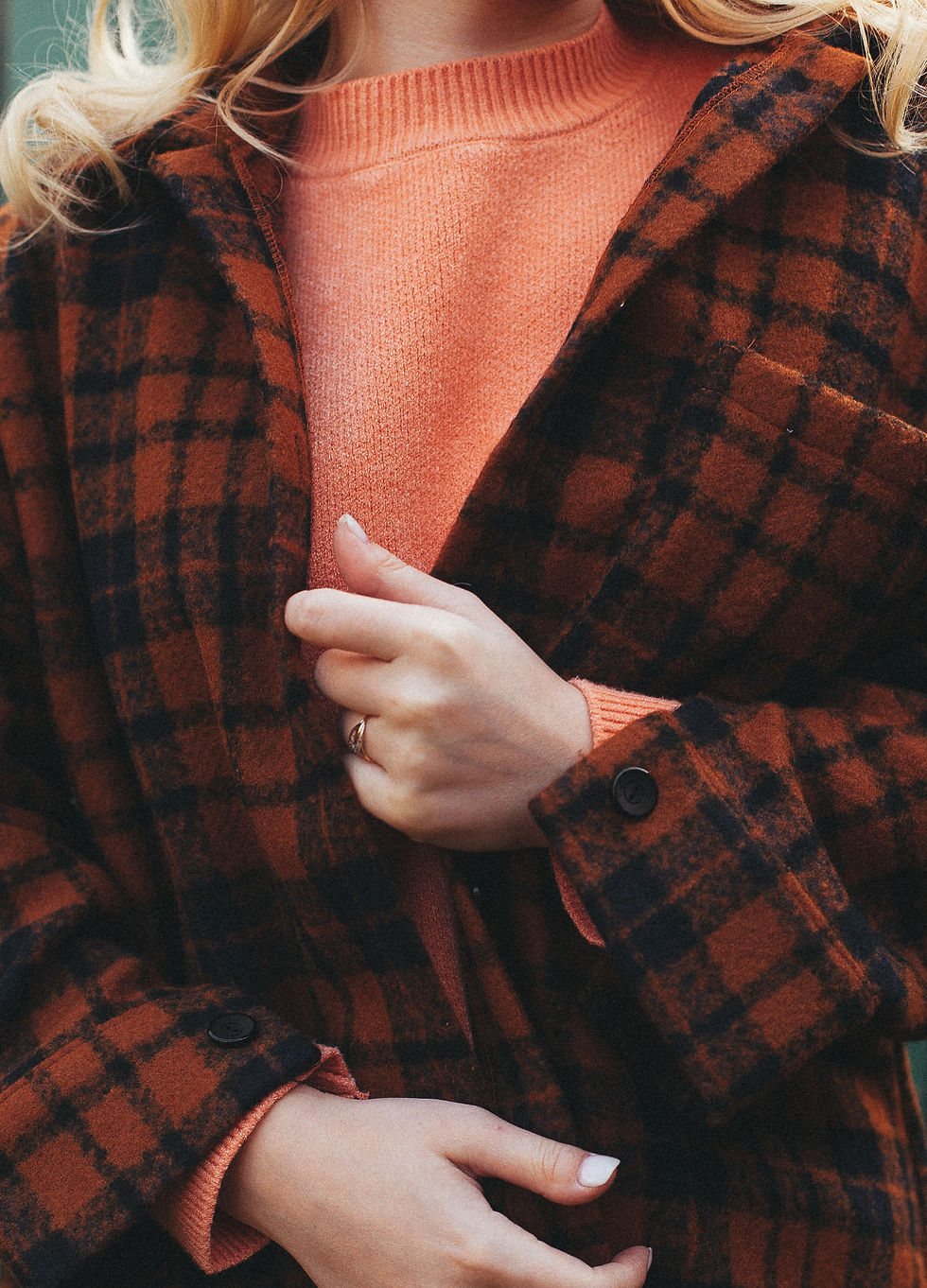 Close-up of a brown checked coat worn over an orange knit