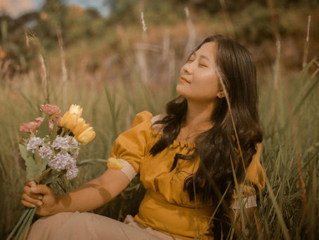 vintage cottagecore aesthetic - a woman lies in long grass holding a bunch of wild flowers with her eyes closed, enjoying the autumnal sun
