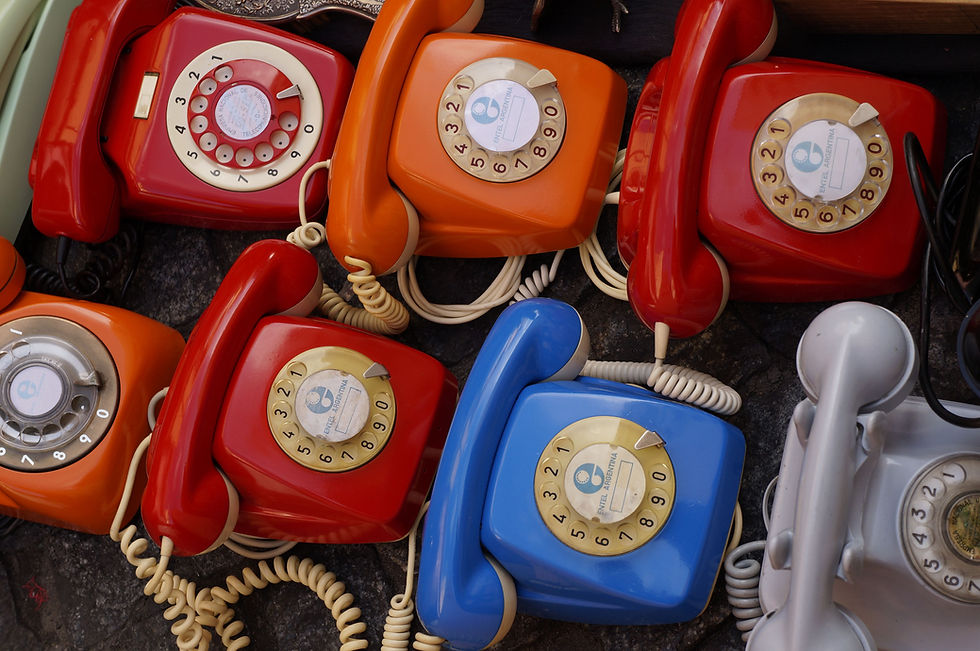Colourful vintage rotary dial phones in red, orange, blue and grey lined up together.