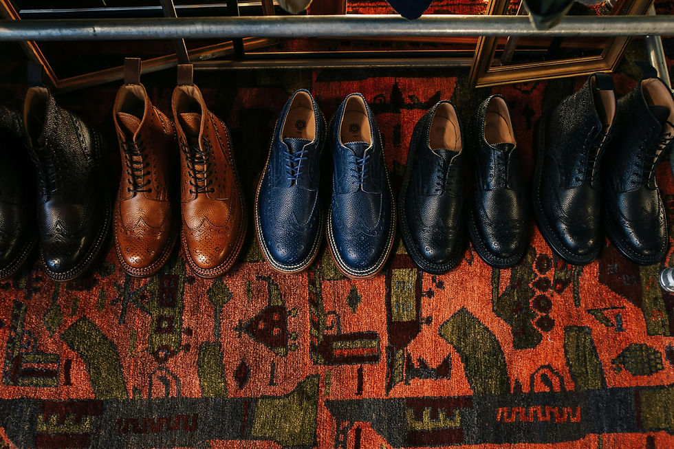 Row of mens leather shoes in various styles and colours (black, brown, blue) on a textured, multicoloured patterned carpet.