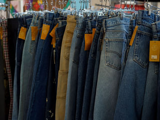 Rows of blue and tan vintage jeans on hangers in a clothing store, with orange tags hanging from waistbands.
