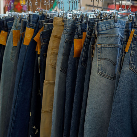 Rows of blue and tan vintage jeans on hangers in a clothing store, with orange tags hanging from waistbands.