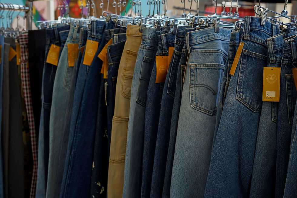 Rows of blue and tan vintage jeans on hangers in a clothing store, with orange tags hanging from waistbands.