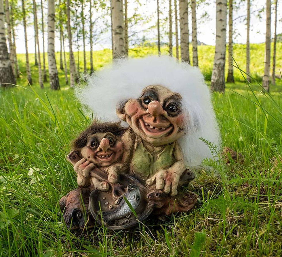 Two Nyform troll figurines with white and dark hair sit in grass in a birch forest.