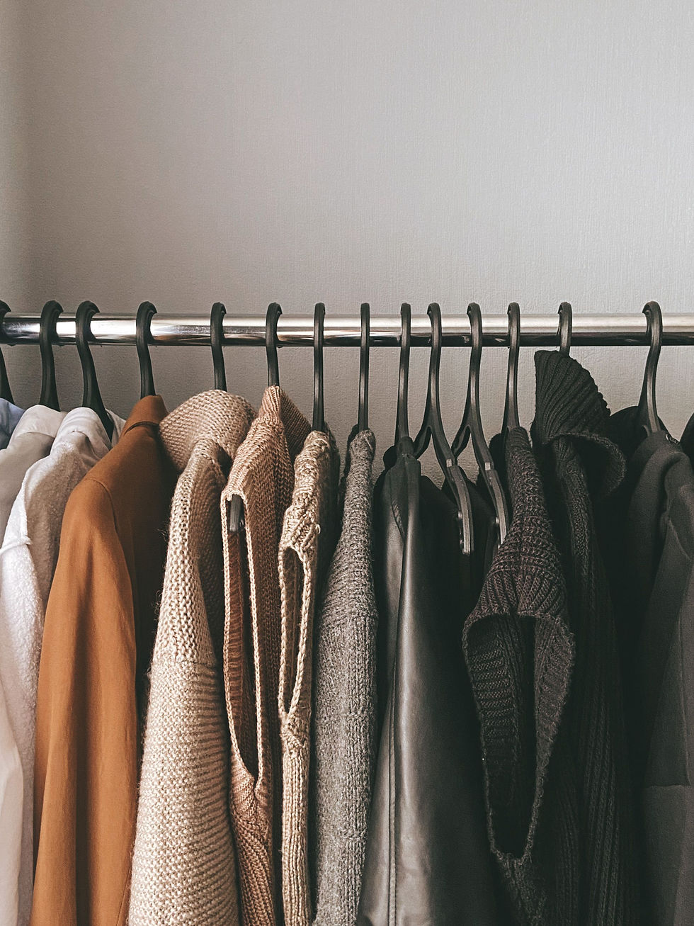 Curated knitwear and classic wardrobe pieces arranged on a clothing rail in neutral and earthy tones.