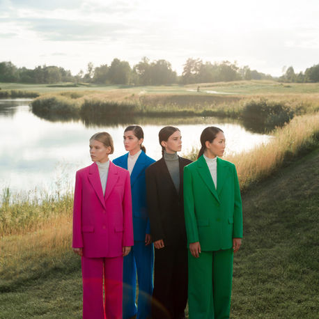 Four women wearing colourful tailored trouser suits outdoors