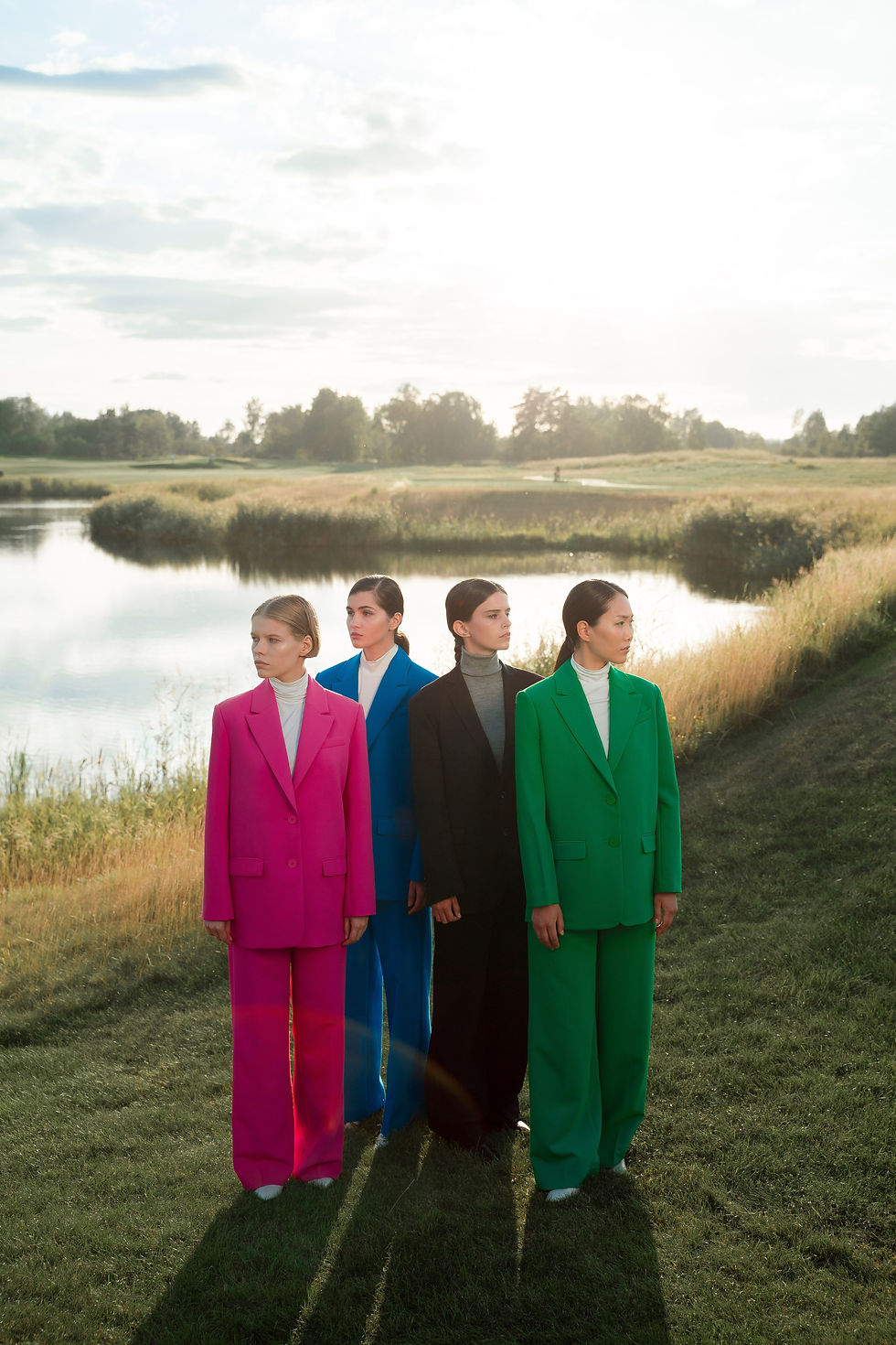 Four women wearing colourful tailored trouser suits outdoors