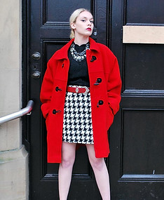 Woman wears vintage outfit with vintage red coat, vintage black top and vintage houndstooth mini skirt. Standing infront of a large black door, confidently. Vintage clothing | Womens Vintage | Vintage Fashion
