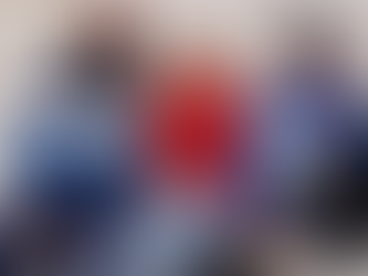 Three people in colorful sporty jackets sit casually against a concrete wall. They wear caps and display logos like Nike and Champion.