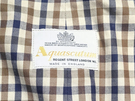 Close-up of blue, brown, and cream plaid fabric with a white Aquascutum label reading Made in England