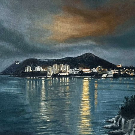 Night view across Tai Tam Bay to Stanley, Hong Kong, with glowing lights reflected on the water beneath dark hills.