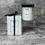 Thumbnail: Clear candle jar with black lid sitting next to a white box packaging with black ribbon ties into a bow on a concrete top