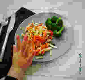 Main d'enfant qui repousse son assiette pleine de légumes.