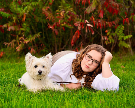 Class of 2024 high school senior portrait of a young woman and her dog laying in the grass. Photography by Bonni Allen.