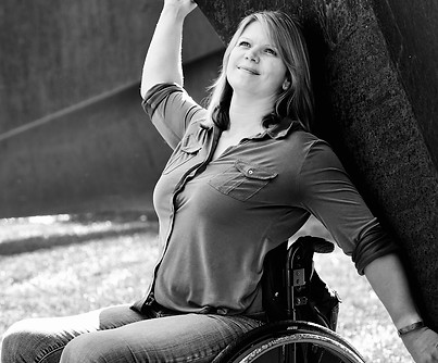 Lifestyle portrait in St Paul, MN of Regan Linton, sitting in a wheelchair with her arms stretched out and smiling.