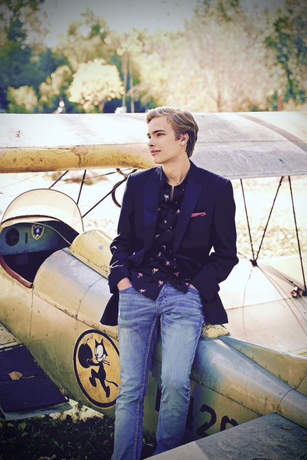 High school senior portrait of a young man in jeans and a blazer leaning against a plane in the Twin Cities. Photo credit Bonni Allen.